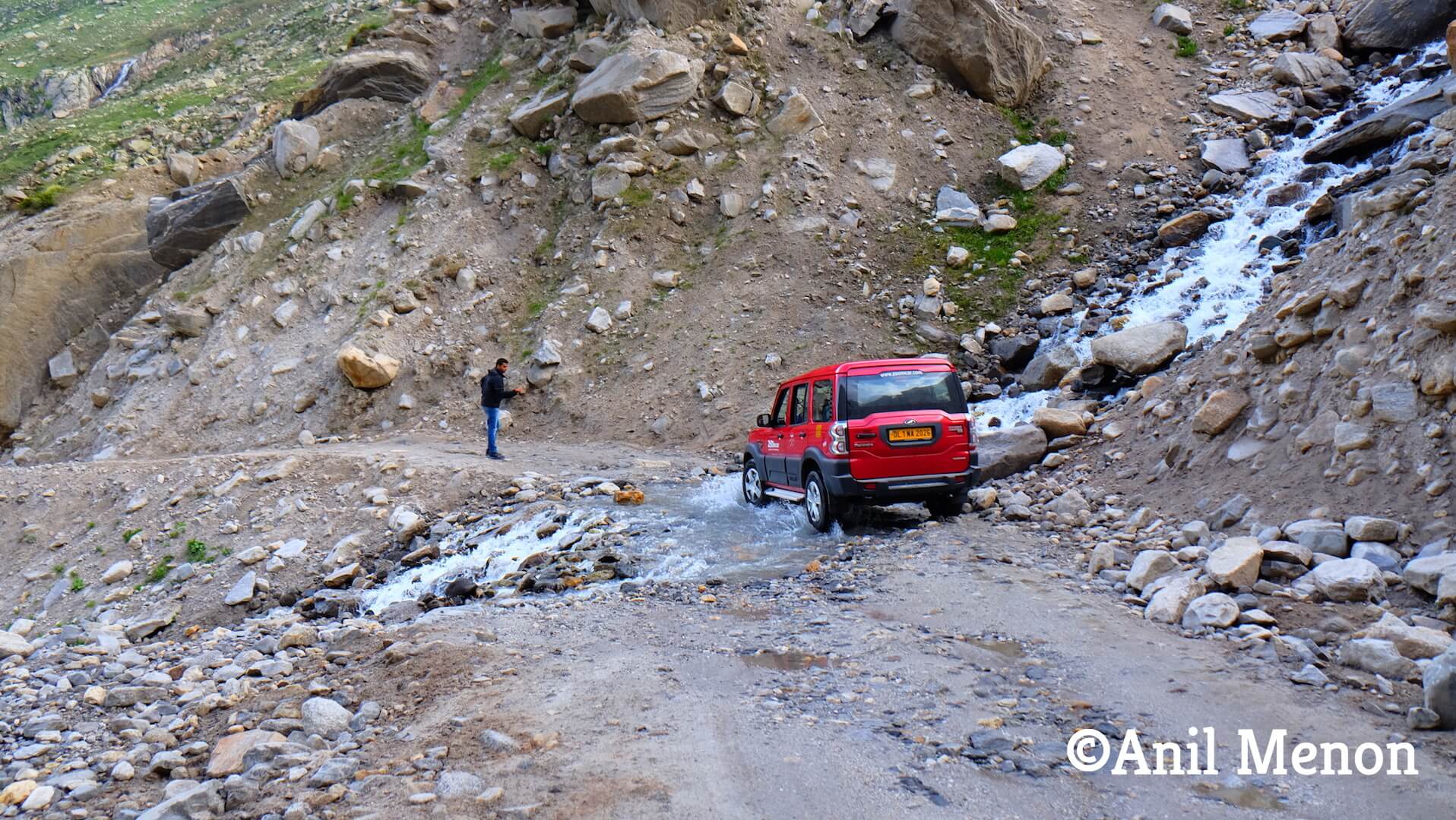 A red car navigating through a stream and bad roads