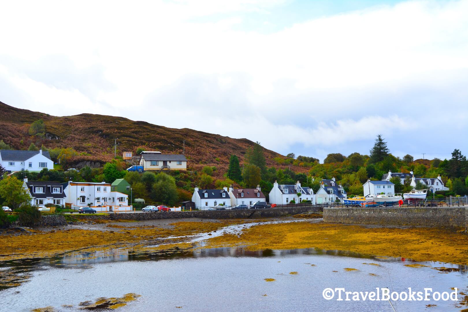 Lots of white houses amidst fall foliage with a water body in front of them and a mountain behind them in Kyleakin, Scotland