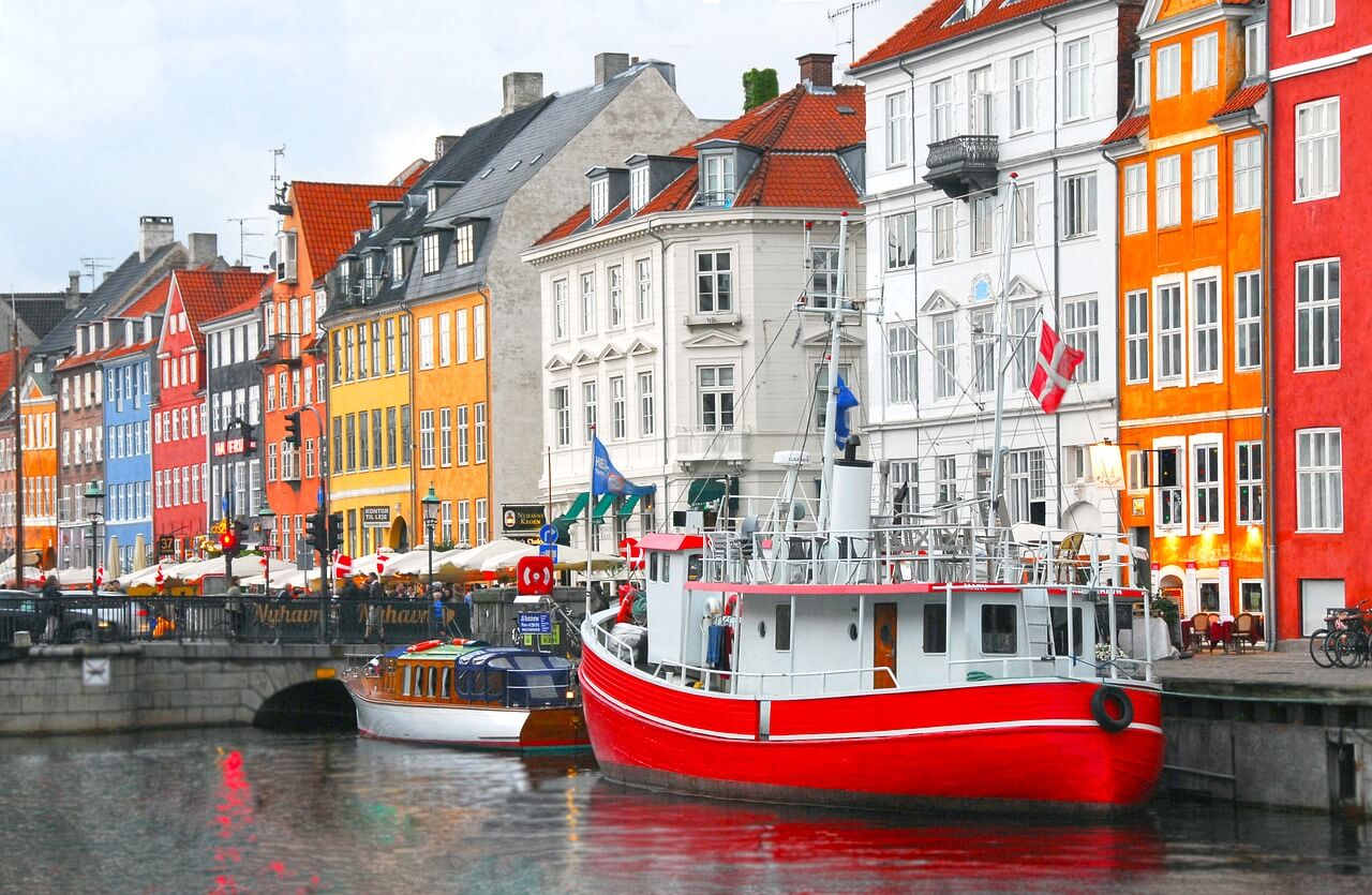 A row of colourful houses with a harbour and couple of boats in front of them in Copenhagen, Denmark