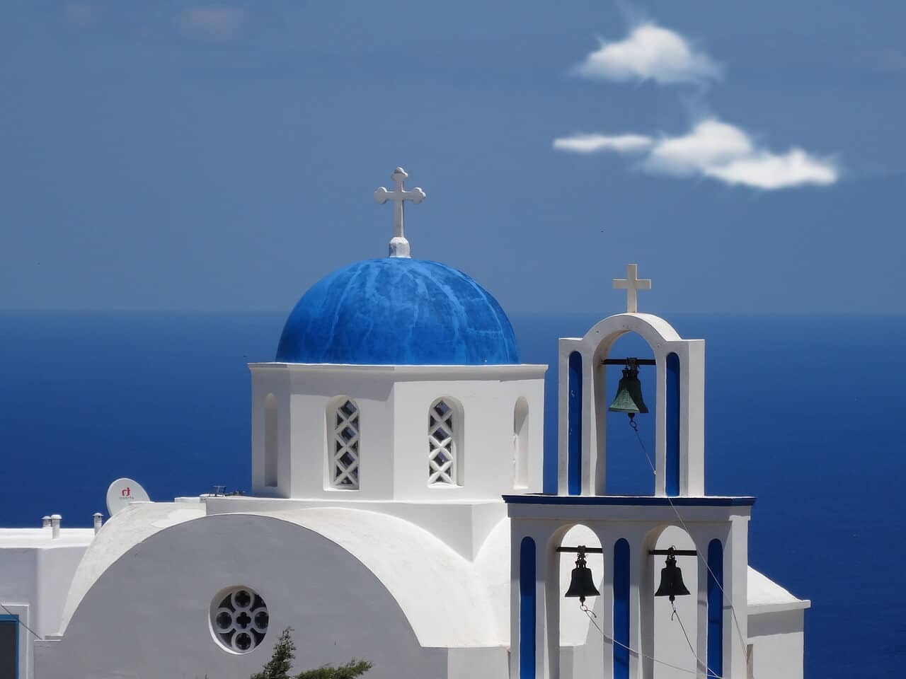 A photo of a white church with a blue dome with the sea in the background in Santorini, Greece