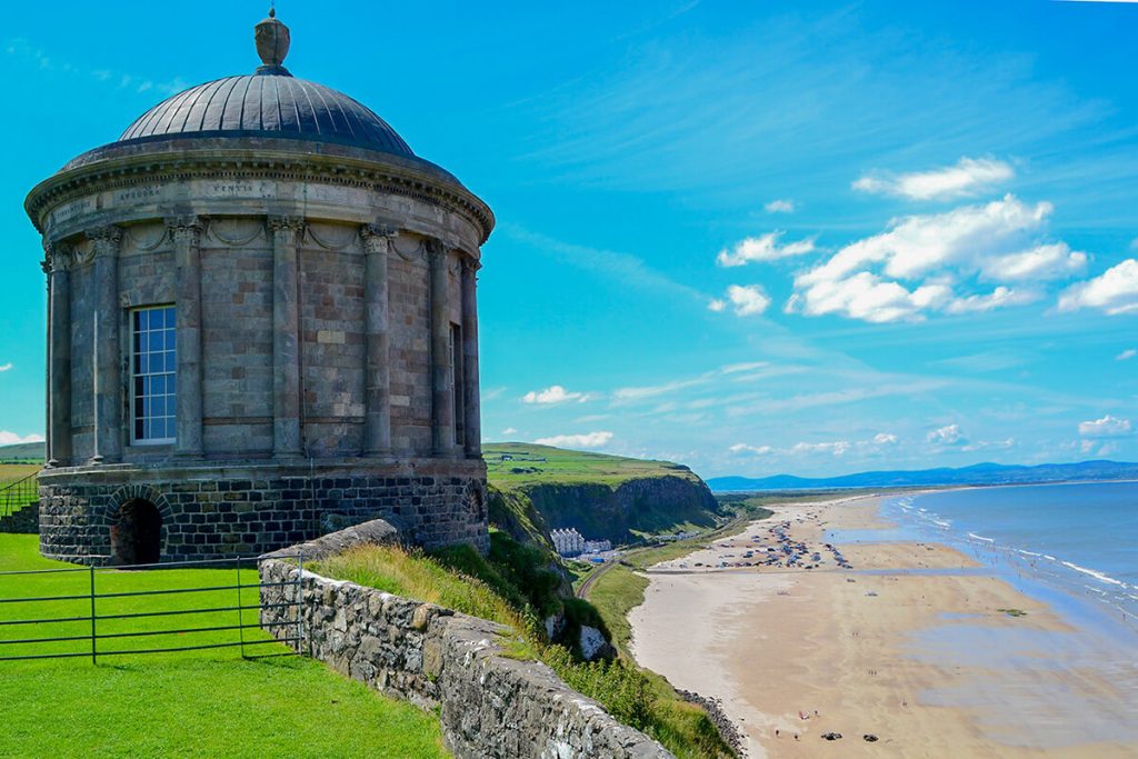 A photo of a building with a round dome on a cliff besides a sandy beach in Northern Ireland