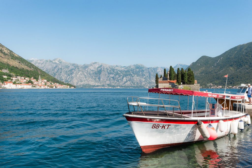 A photo of a white boat with an island in the distance surrounded by mountains on all sides