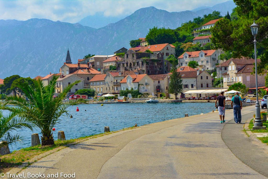 Another photo of the Montenegro coast with a church and some orange tiled buildings set up against the black mountains of Montenegro and clear blue water