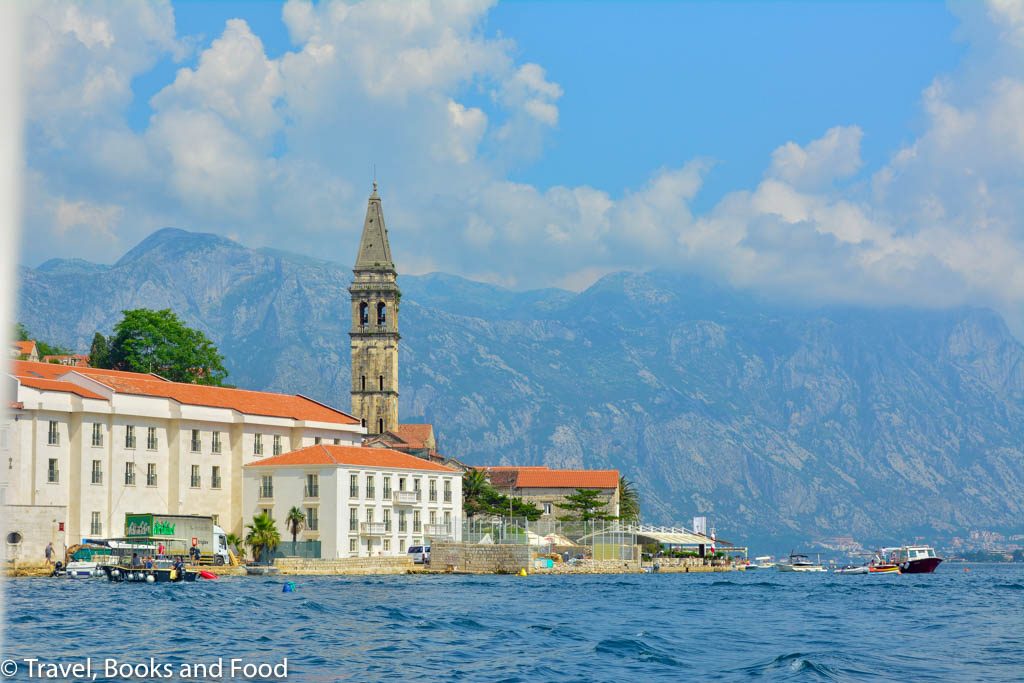 Another photo of the Montenegro coast with a church and some orange tiled buildings set up against the black mountains of Montenegro and clear blue water